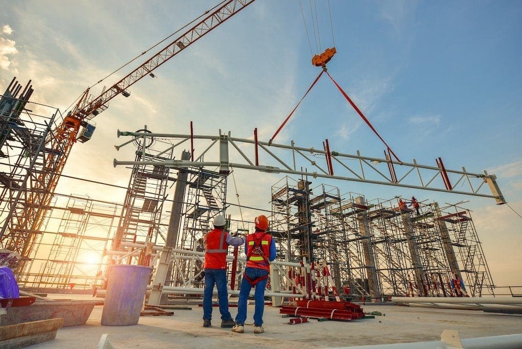 two construction workers standing under crane on job site determining pre-engineered metal buildings average cost