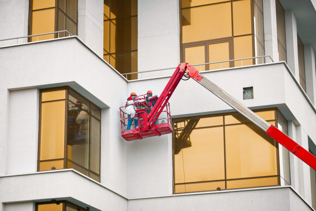 Construction workers working at height in lifting bucket; commercial renovation costs