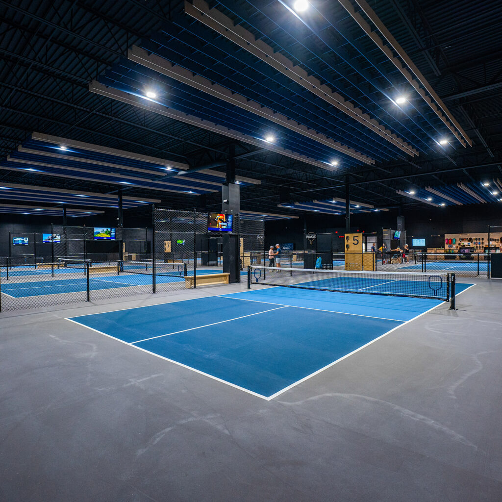 Indoor tennis court with professional-grade flooring, lighting, and fencing for sports and recreatio.