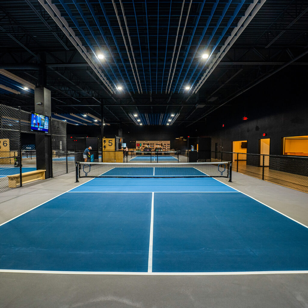 Indoor tennis court with modern lighting and seating areas.